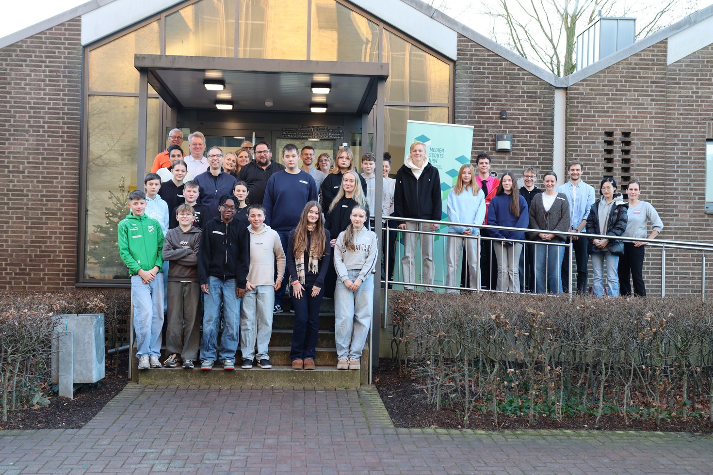 Eine Gruppe aus Jugendlichen und Erwachsenen steht auf der Treppe und einer Rampe vor einem Haus.