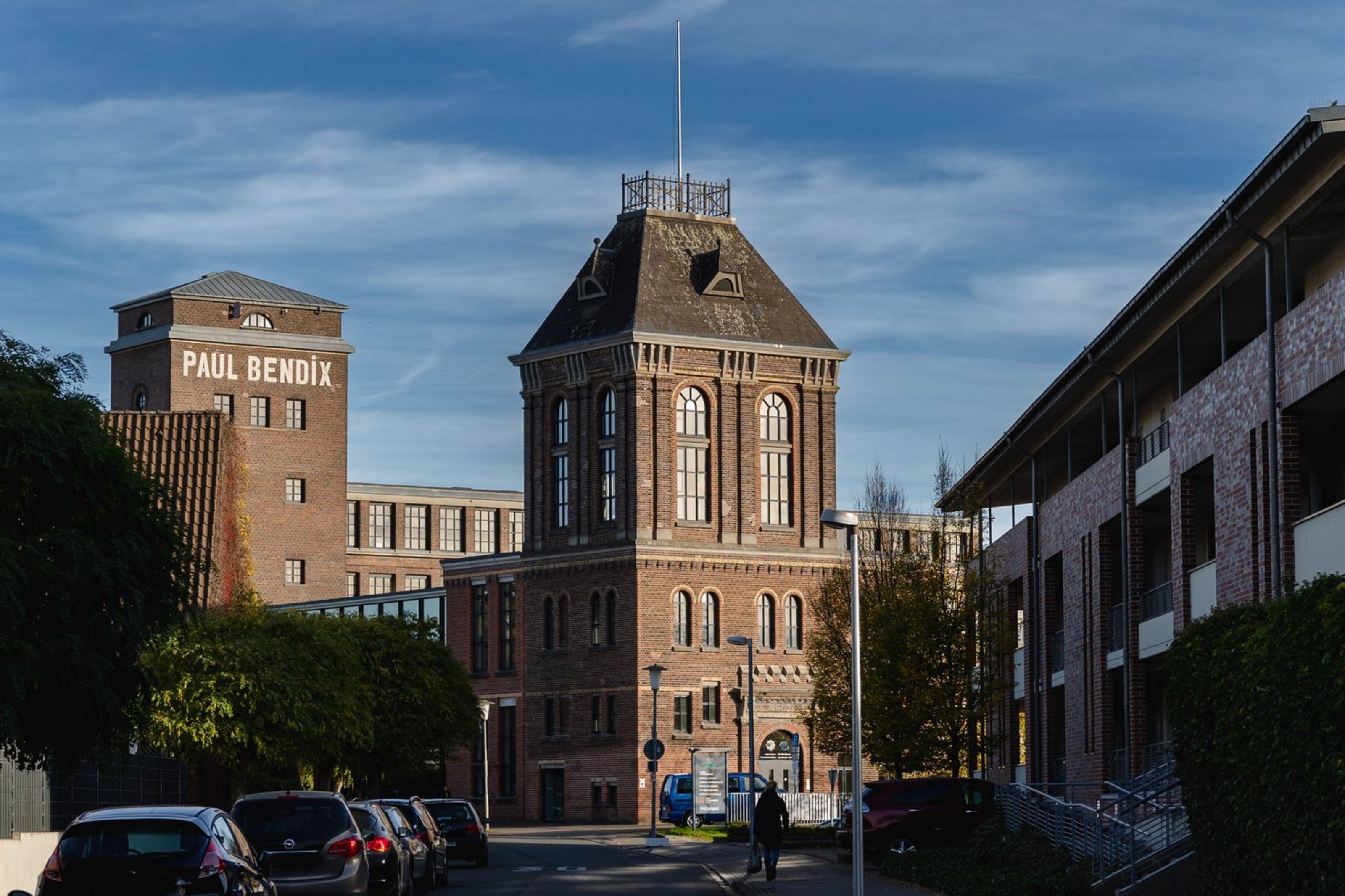 Blick auf ein historisches Backsteingebäude mit Turm vor blauem Himmel und umliegenden modernen Gebäuden