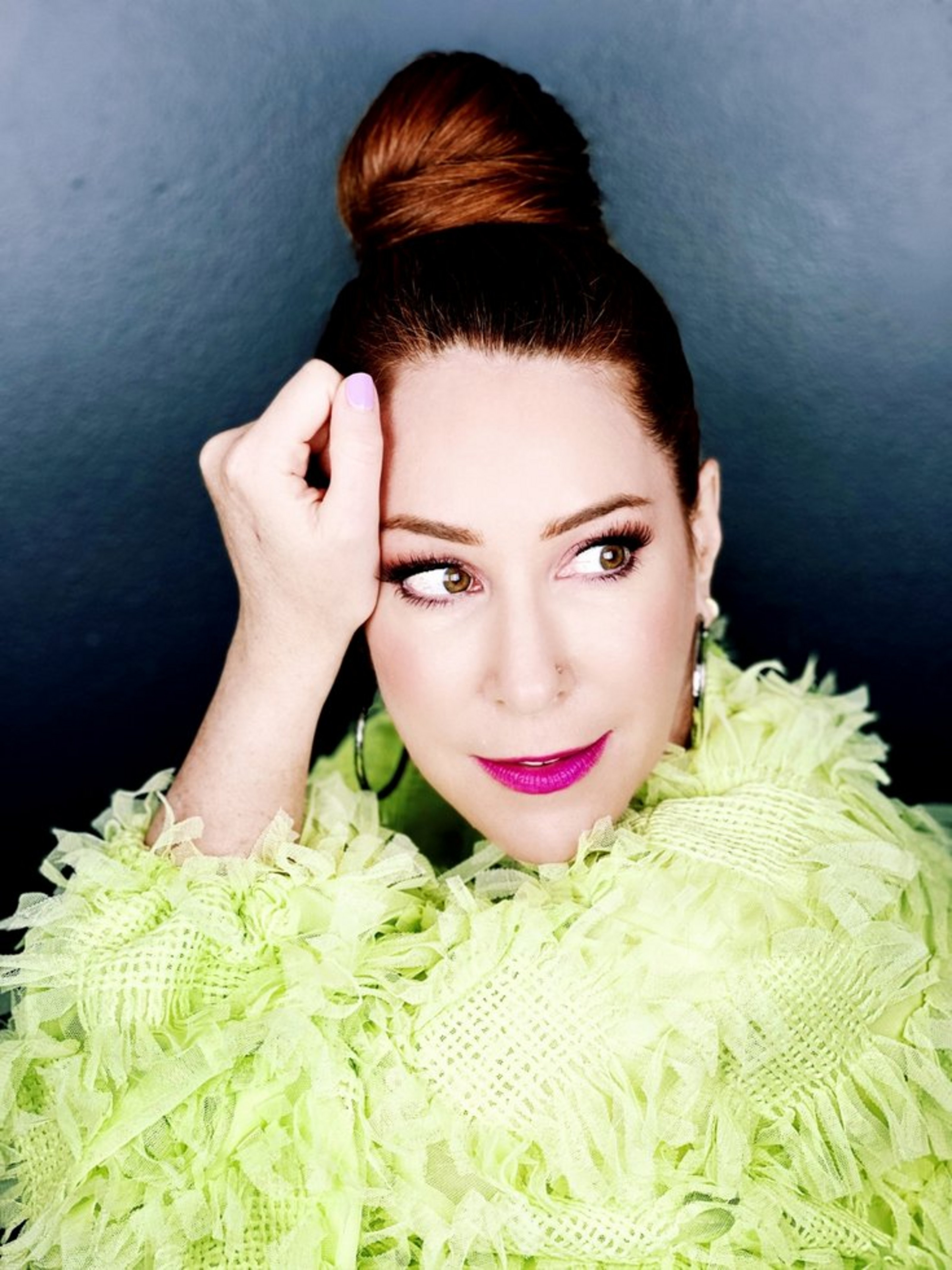 Eine Frau mit grünem, plüschigem Oberteil und roten Haaren, die zu einem Dutt hochgesteckt sind.