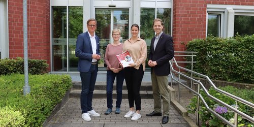 Vier Personen stehen auf einer Treppe und halten den Gesundheitsbericht  in der Hand.