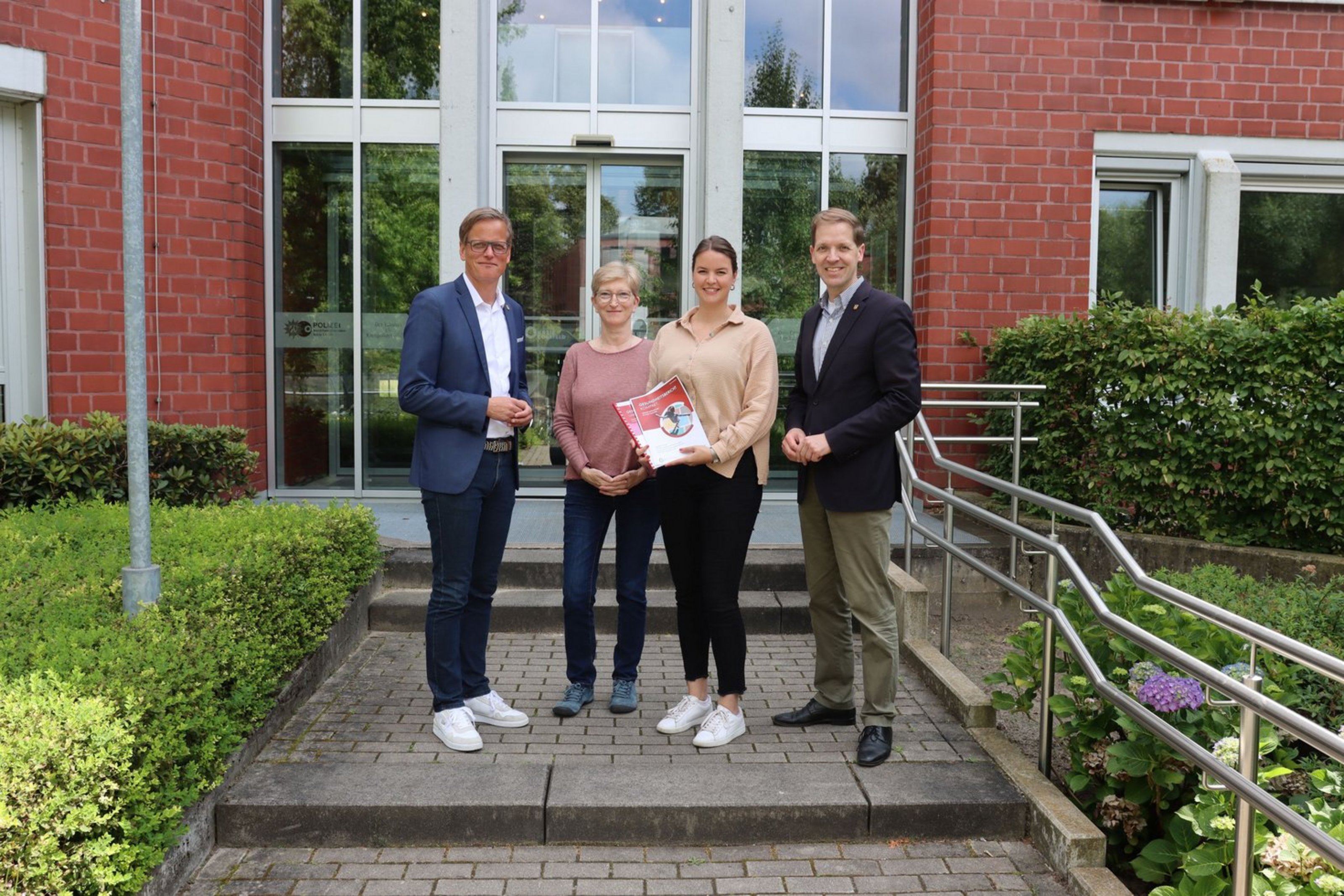 Dezernent Alexander Ruhe, Alexandra Winkler, Leiterin des Gesundheitsamtes, Inga Aschhoff, Mitarbeiterin des Gesundheitsamtes, und Landrat Dr. Christian Schulze Pellengahr (v.l.n.r.) mit dem Gesundheitsbericht (Foto: Kreis Coesfeld). Vier Personen stehen auf einer Treppe und halten den Gesundheitsbericht in der Hand.