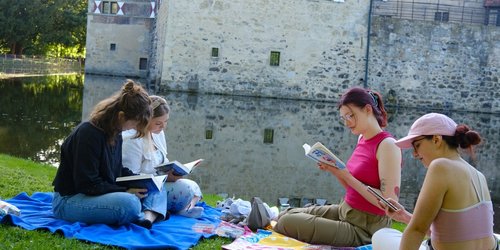 Vier Personen sitzen mit Büchern auf Picknickdecken vor der Burg Vischering und lesen gemeinsam.
