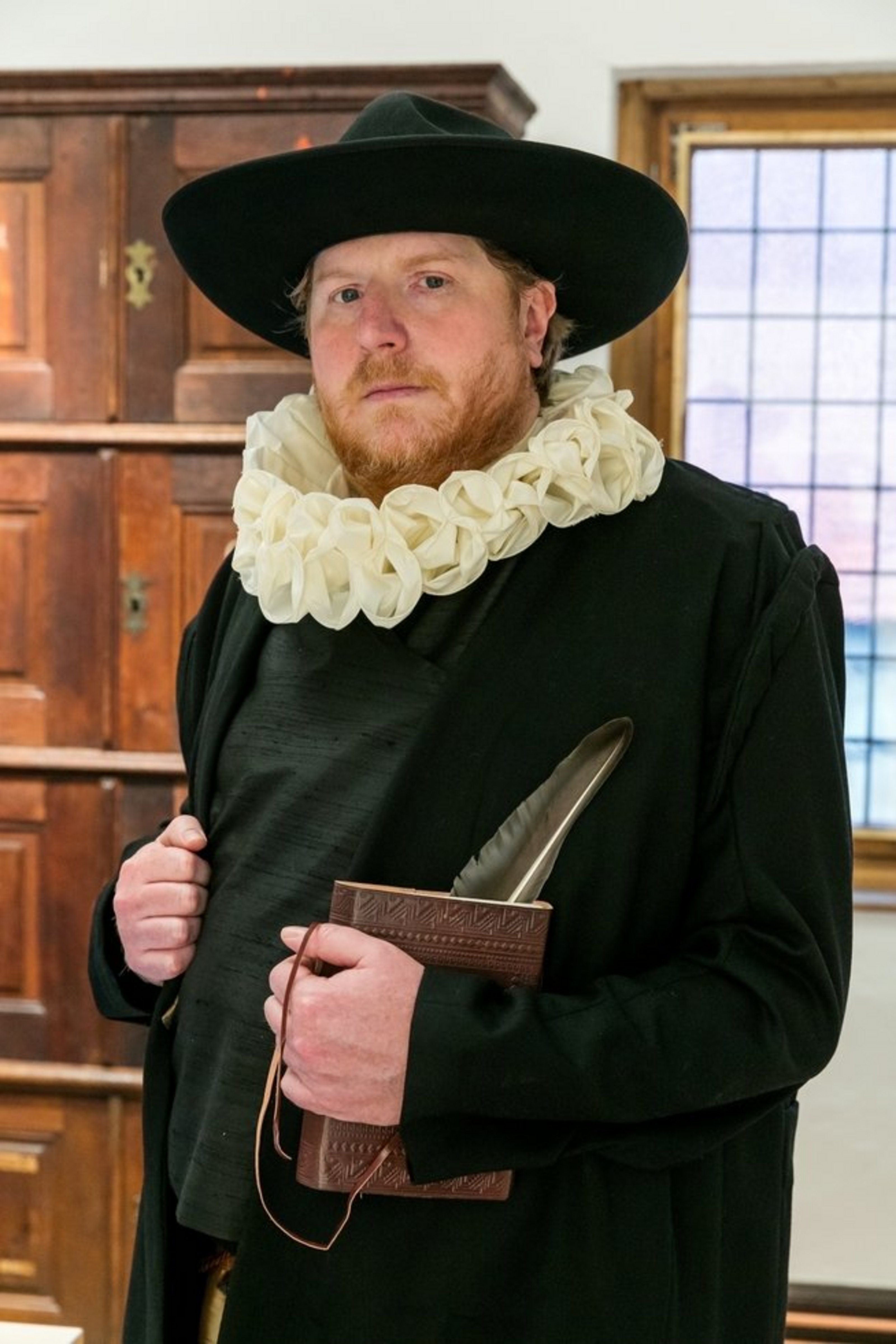 Ein Mann mit historischer, schwarzer Kleidung, Hut und Halskrause blickt in die Kamera.