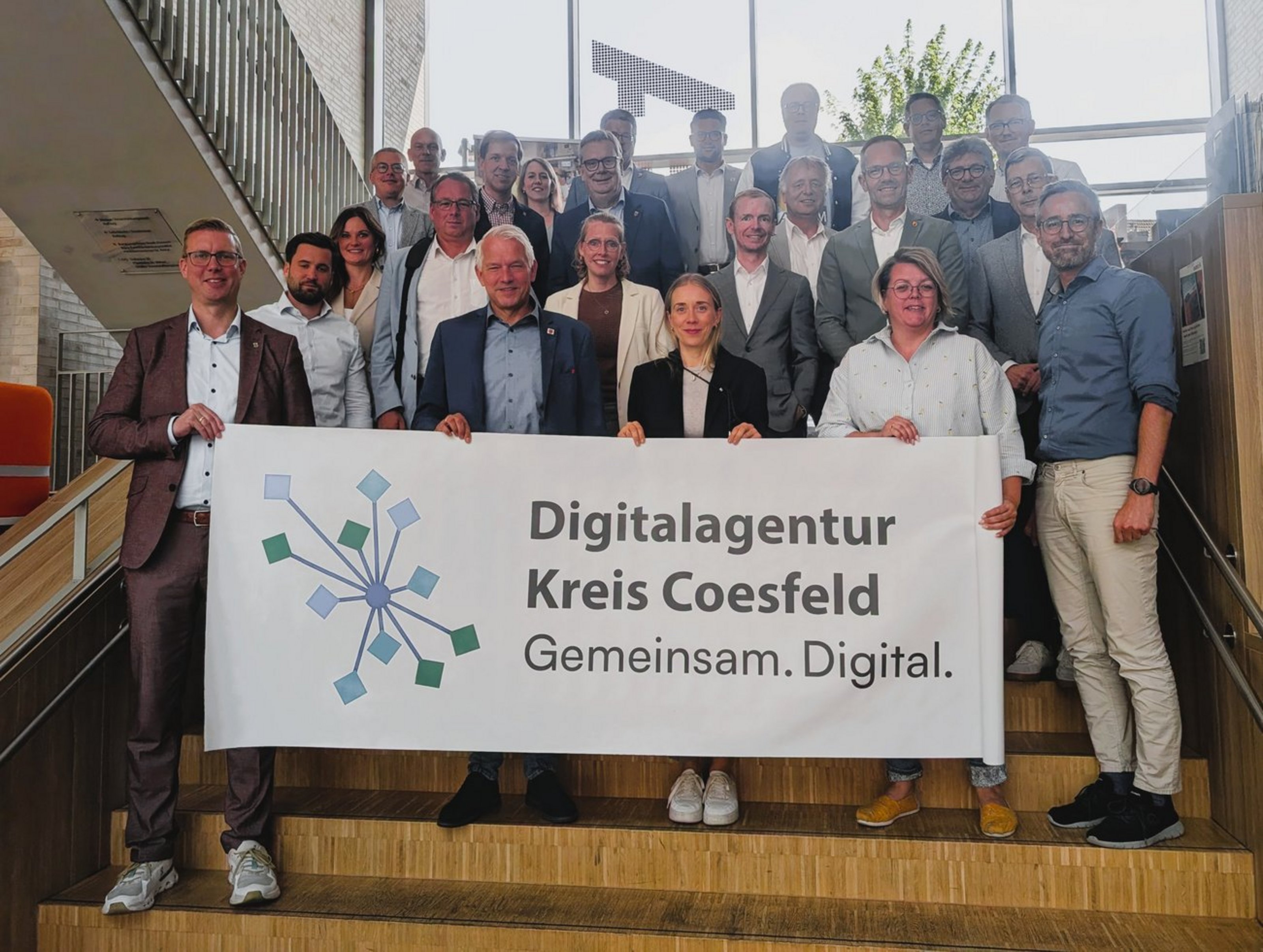 Eine Gruppe von Männern und Frauen steht auf einer Treppe. Sie halten ein großes Schild mit der Aufschrift Digitalagentur Kreis Coesfeld.