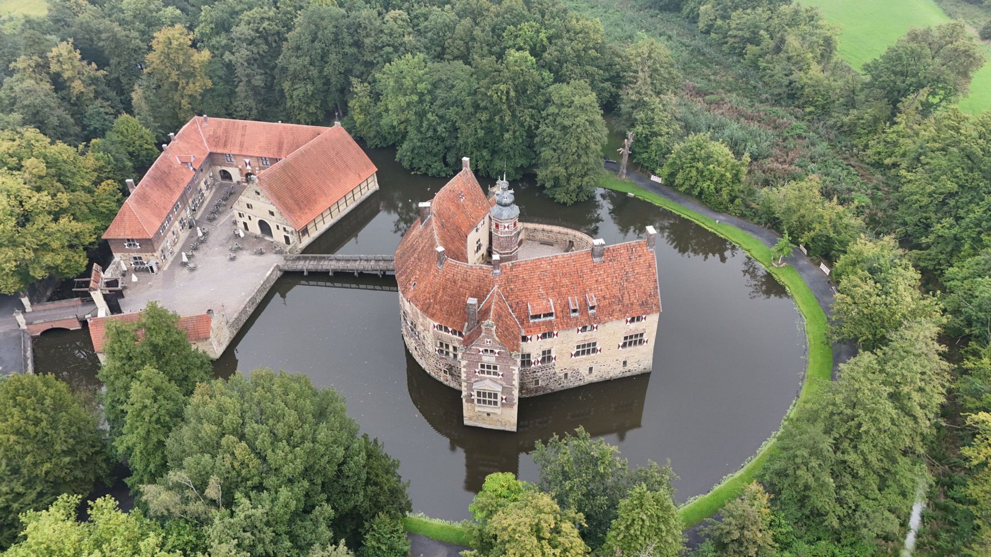 Burg Vischering in Lüdinghausen (Foto: Kreis Coesfeld) Luftaufnahme einer Burg mit Wassergraben, umgeben von grüner Landschaft.