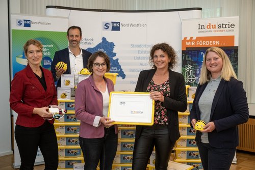 Fünf Personen stehen vor Infotafeln, einige halten Baukästen und Lernroboter in den Händen. Eine Kiste mit der Aufschrift „Industrie“ wird gemeinsam präsentiert.