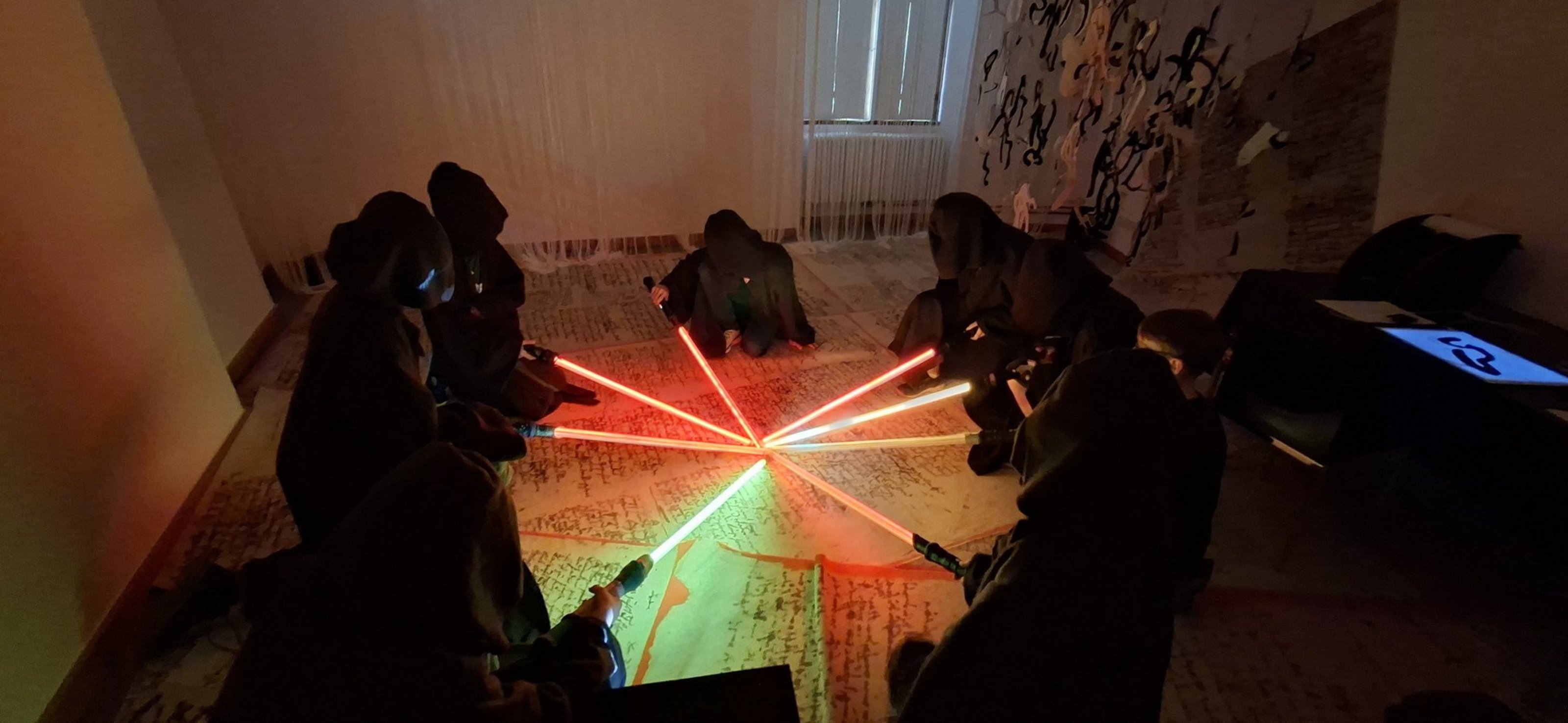 Jugendliche in selbstgemachten Jediroben sitzen mit leuchtenden Lichtschwertern im Kreis auf dem Boden.