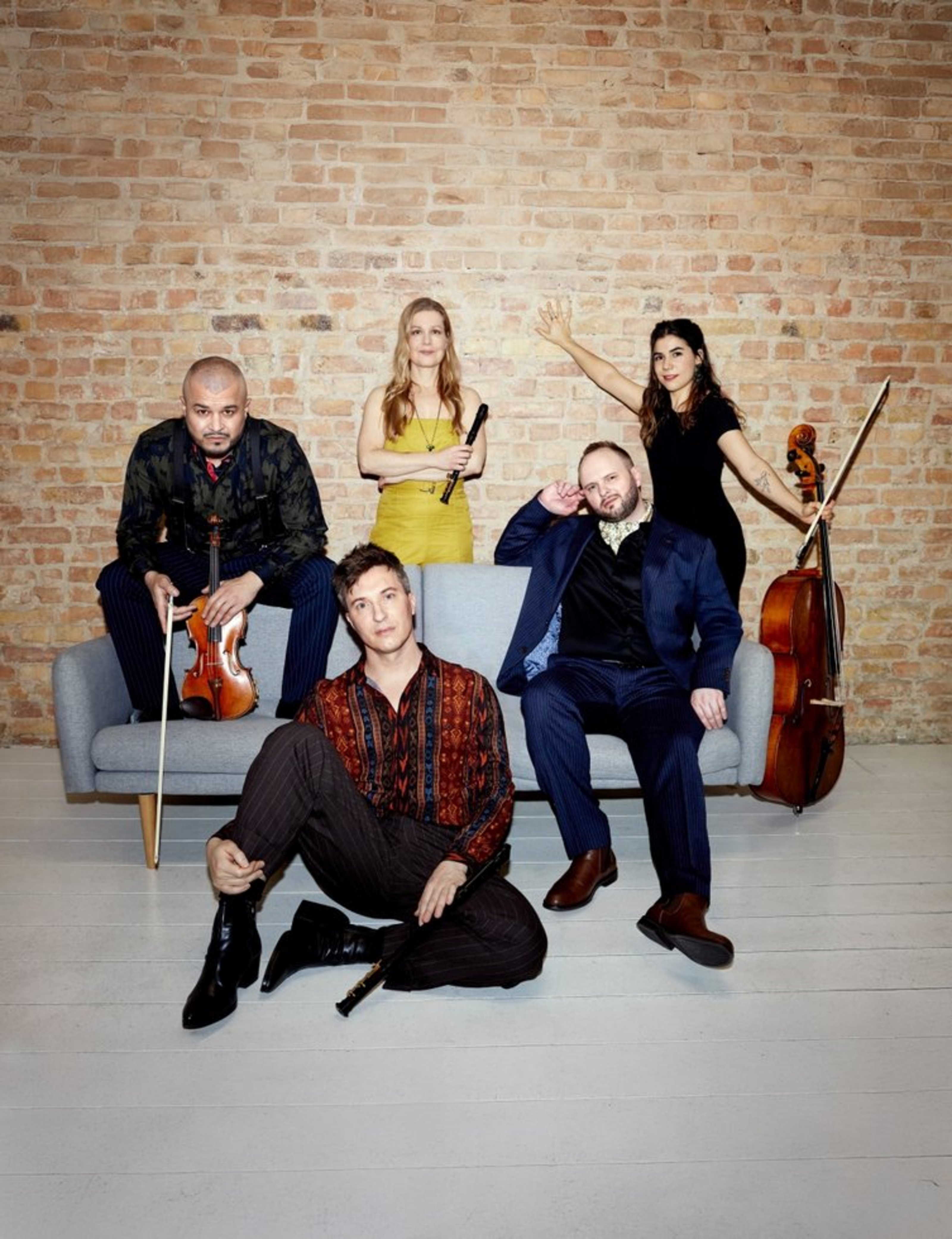 Das Quintett Spark sitzt und steht vor einer Backsteinwand mit Klarinetten und Streichinstrumenten.