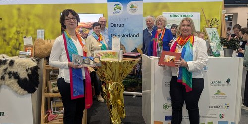 An einem Messestand mit der Aufschrift "Das gute Leben" stehen sechs Personen. Auf einem Banner ist zu lesen "Golddorf Darup im schönen Münsterland".