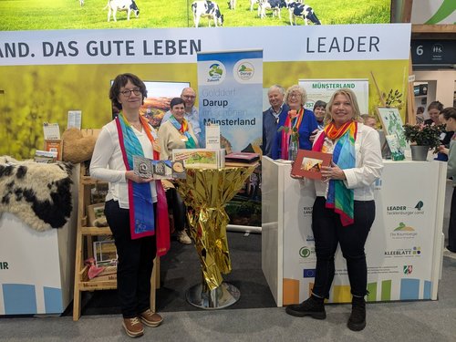 An einem Messestand mit der Aufschrift "Das gute Leben" stehen sechs Personen. Auf einem Banner ist zu lesen "Golddorf Darup im schönen Münsterland".