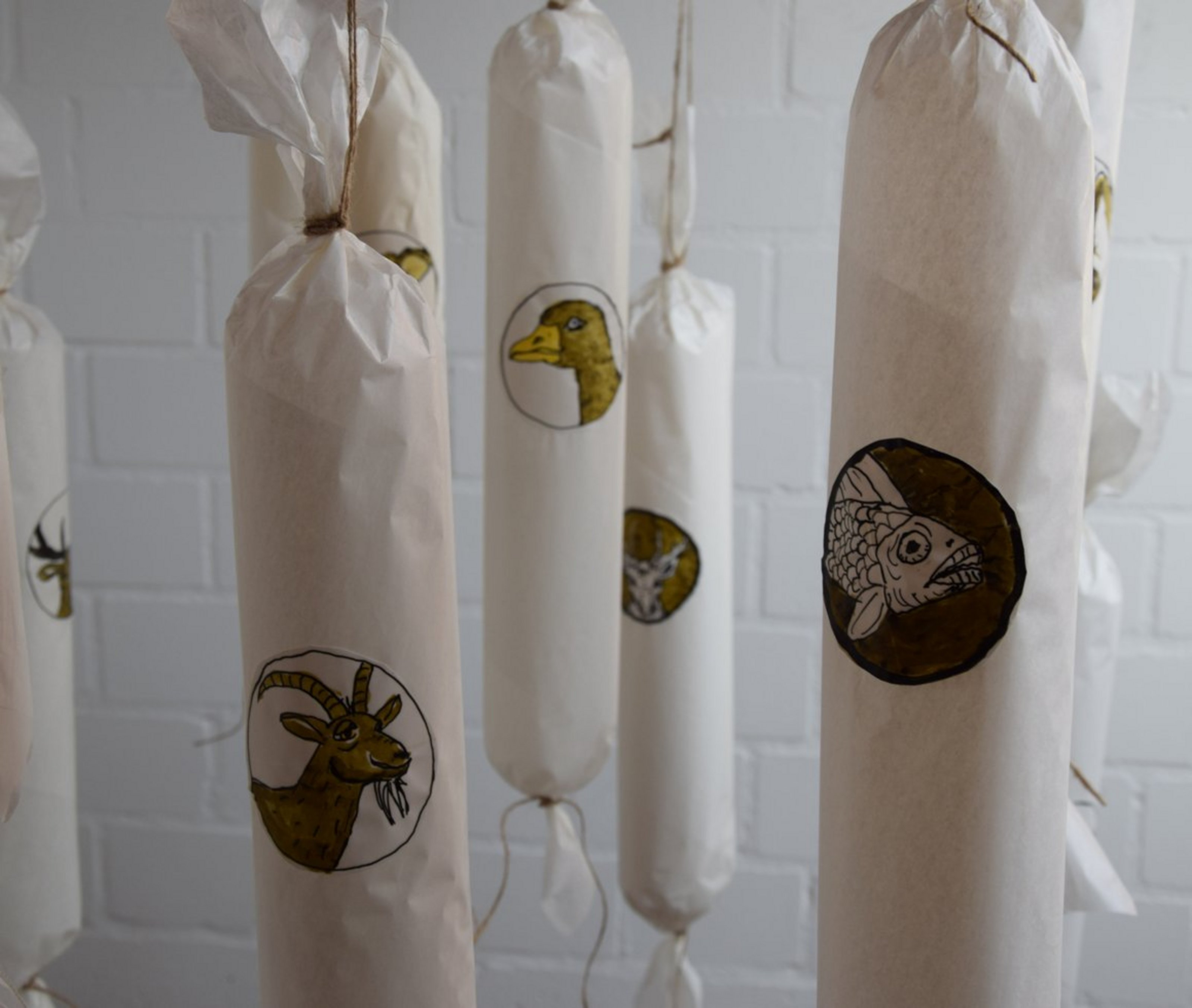 In Papier eingewickelte Würste mit gezeichneten Tiermotiven hängen an Schnüren – Teil des Kunstwerks „Alles Wurst“ von Elisabeth Fellermann.