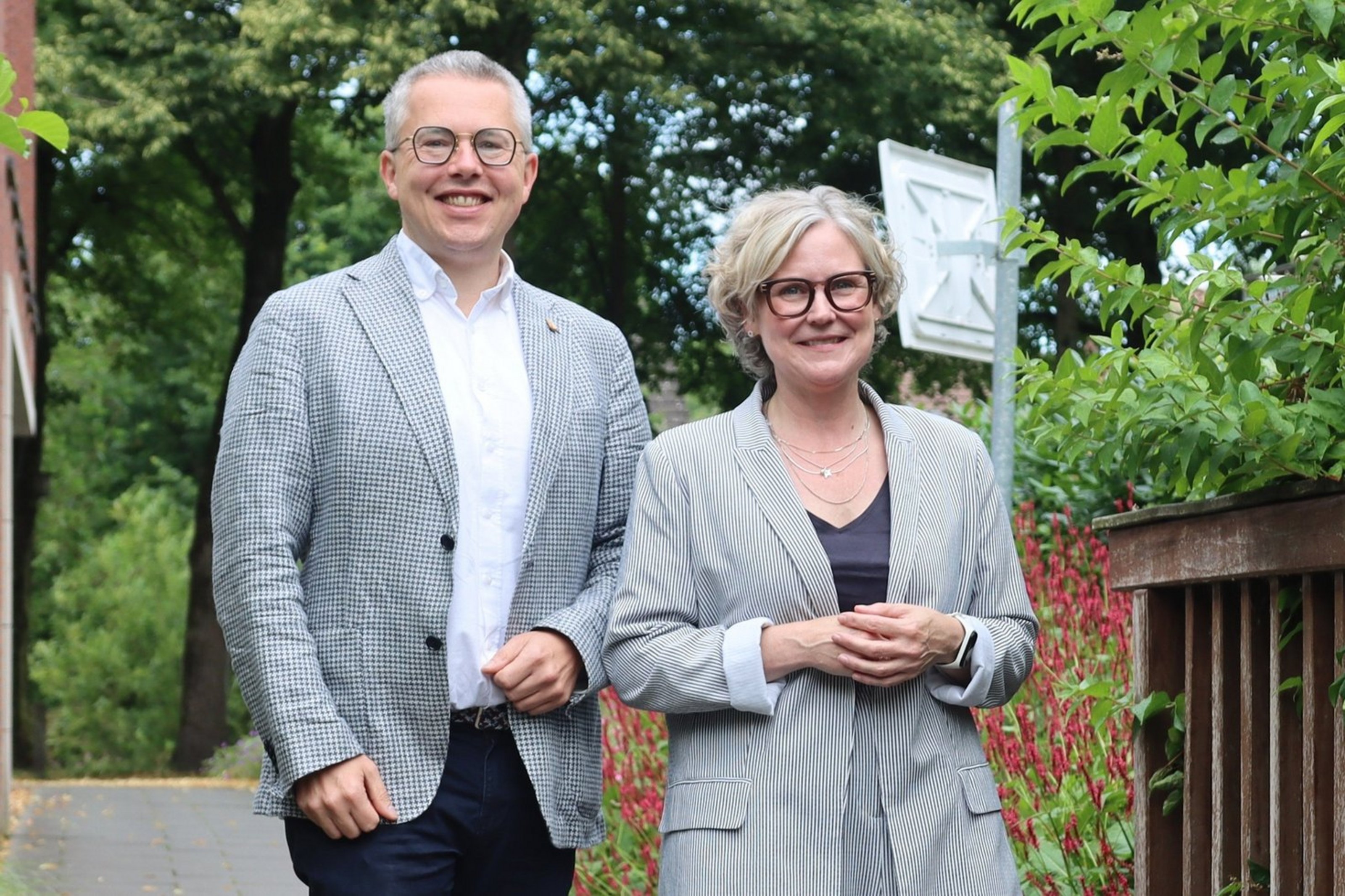 Zwei Personen stehen lächelnd nebeneinander im Grünen vor dem Kreishaus Coesfeld.
