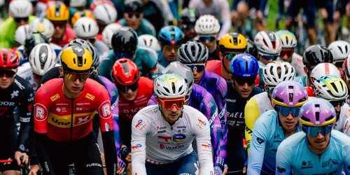 Eine Gruppe von zahlreichen Radfahrern in bunten Trikots, Helmen und Brillen.