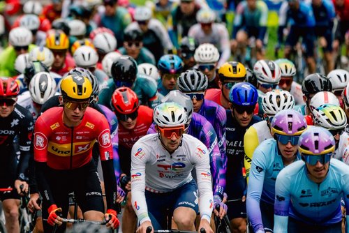 Eine Gruppe von zahlreichen Radfahrern in bunten Trikots, Helmen und Brillen.