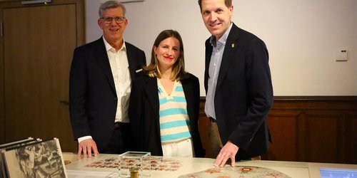 Drei Personen stehen in der Ausstellung der Burg Vischering und präsentieren historische Exponate, darunter ein Petschaftsiegel, das auf einem Tisch vor ihnen liegt.