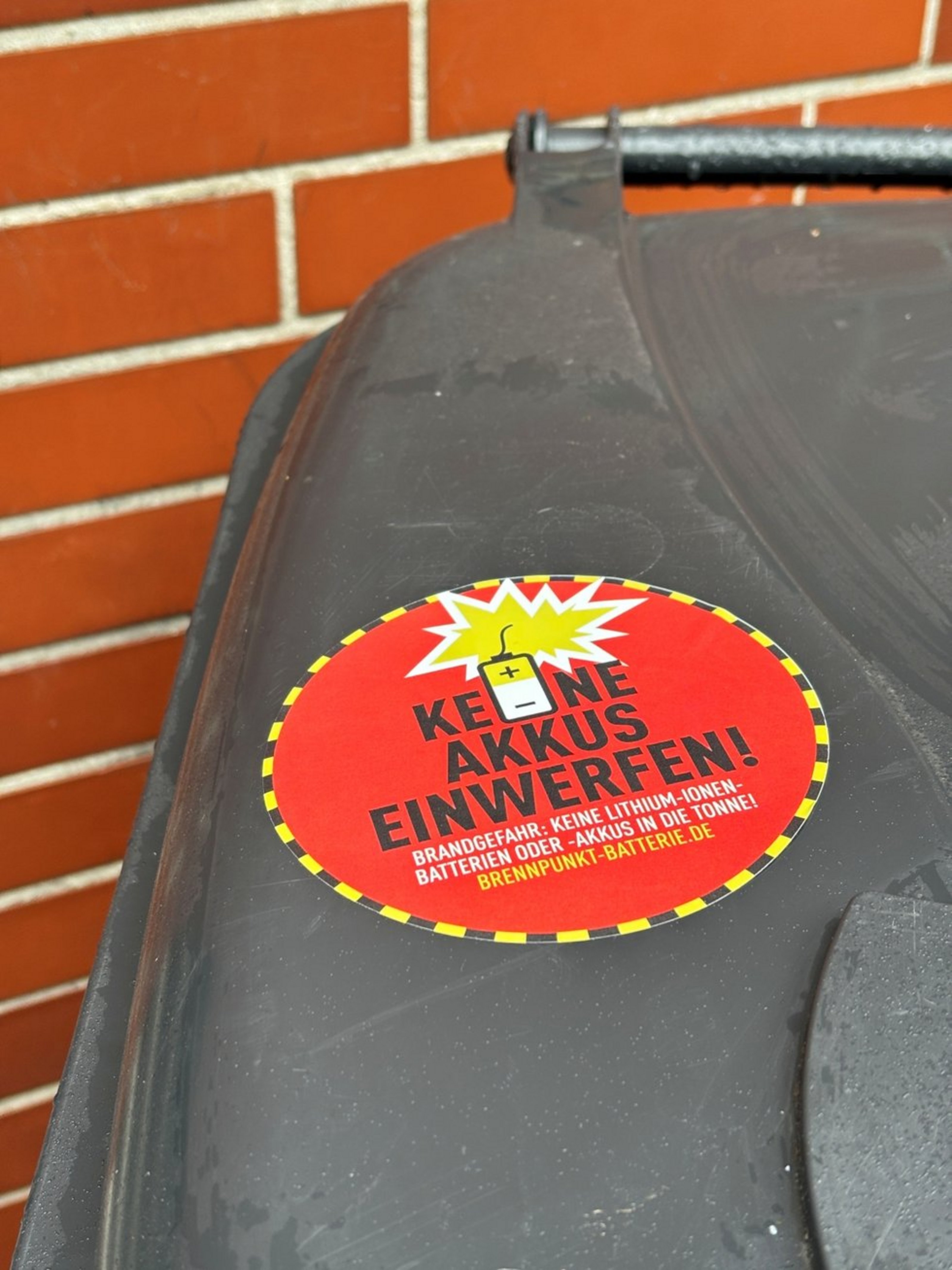 Man sieht den Deckel einer Mülltonne mit einem roten Sticker, auf dem Keine Akkus einwerfen steht.