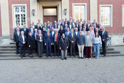 Eine Gruppe von ca.. 60 Personen steht auf den Treppenstufen vor einem alten Backsteingebäude in mehreren reihen hintereinander aufgereiht und schaut in die Kamera.