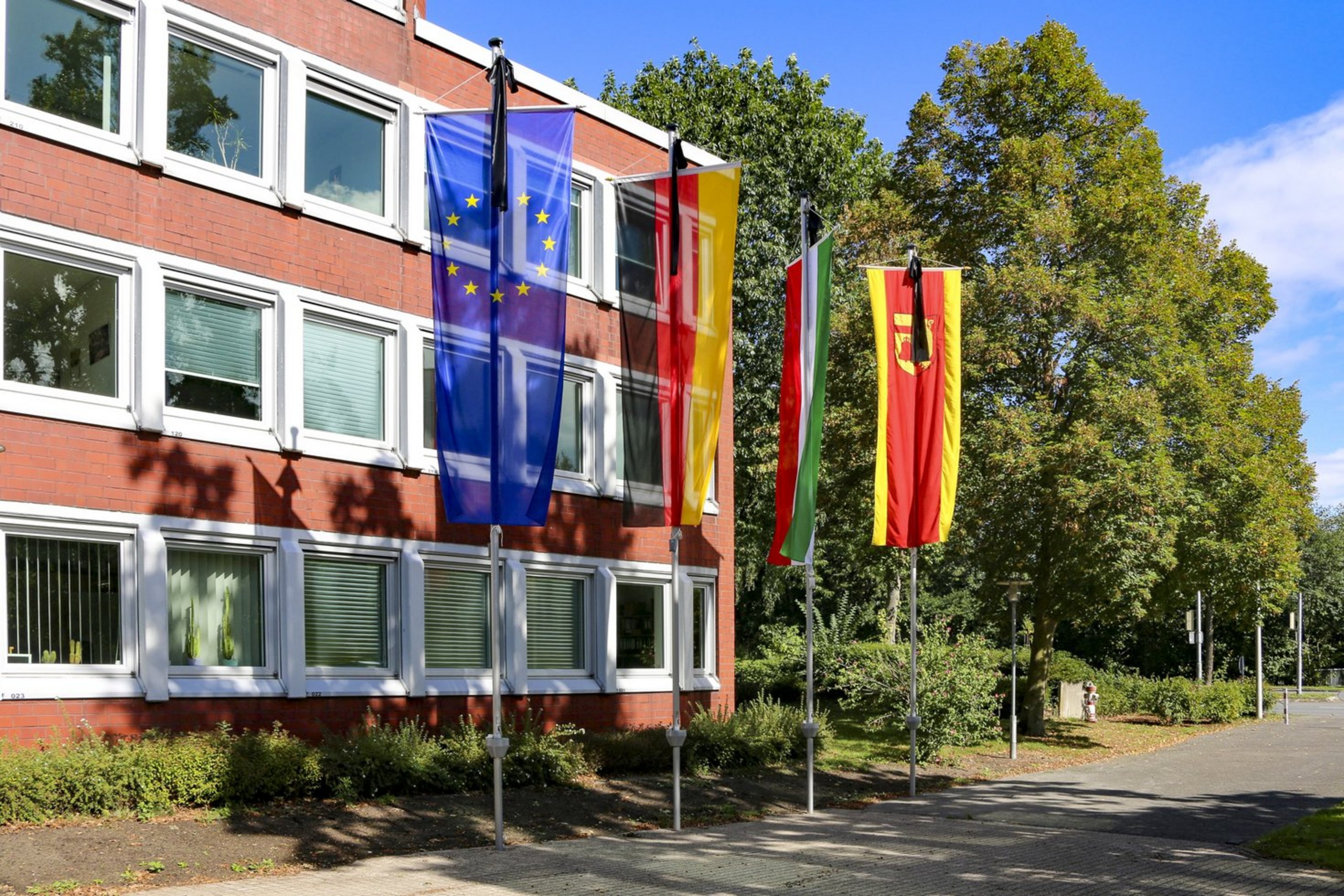 Man sieht vier verschiedene Flaggen, die mit schwarzen Trauerwimpeln versehen sind. Es handelt sich um die Europafahne, die Deutschlandflagge, die Flagge von Nordrhein-Westfalen und vom Kreis Coesfeld.