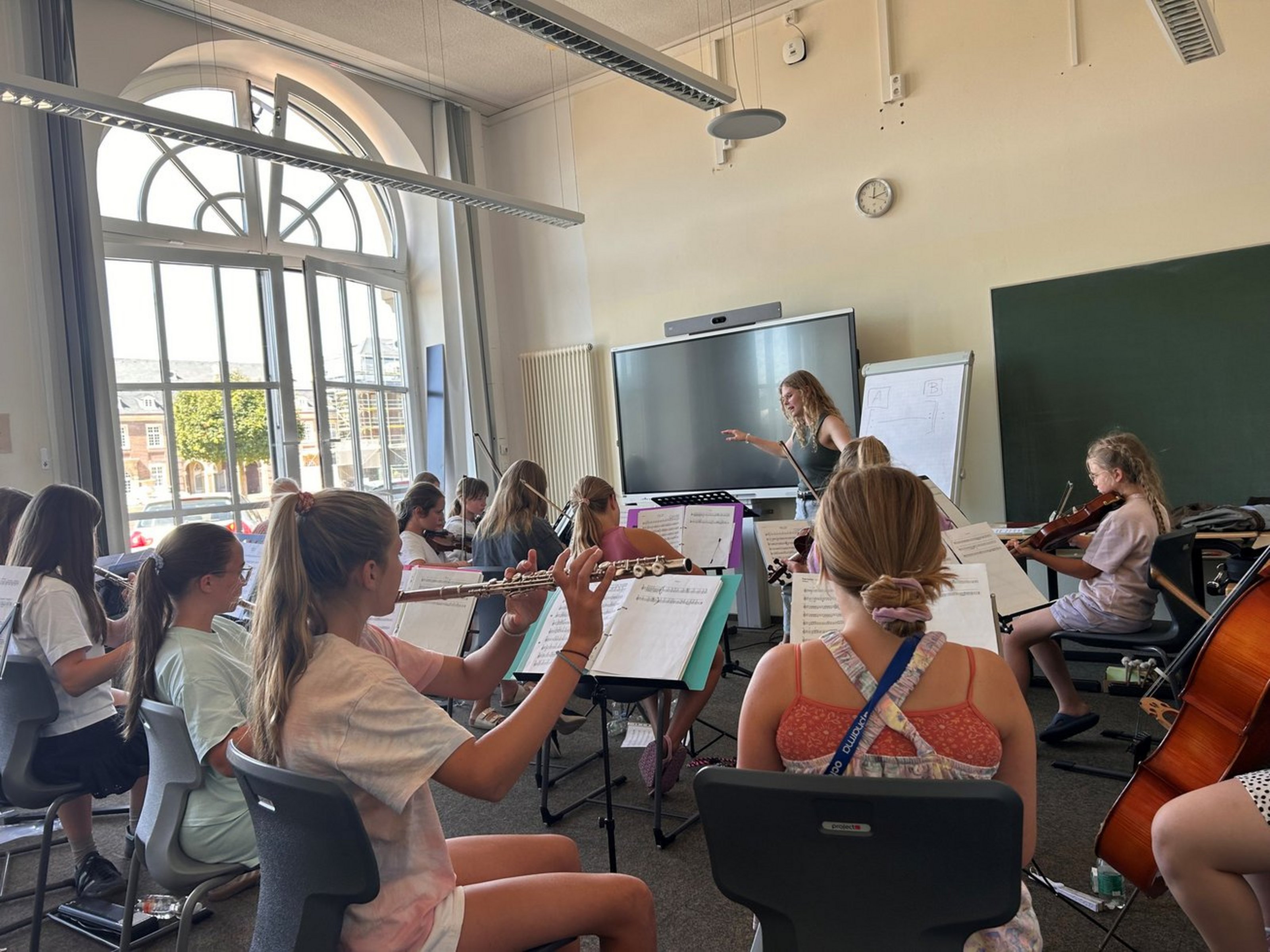 Mehrere Kinder sitzen in einem hellen Raum und spielen auf verschiedenen Instrumenten.