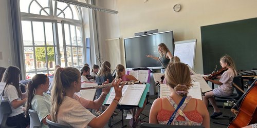 Mehrere Kinder sitzen in einem hellen Raum und spielen auf verschiedenen Instrumenten.