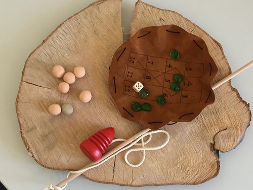 Auf einem Holzbrett liegen Spielsteine, ein Kreisel und ein Beutel .