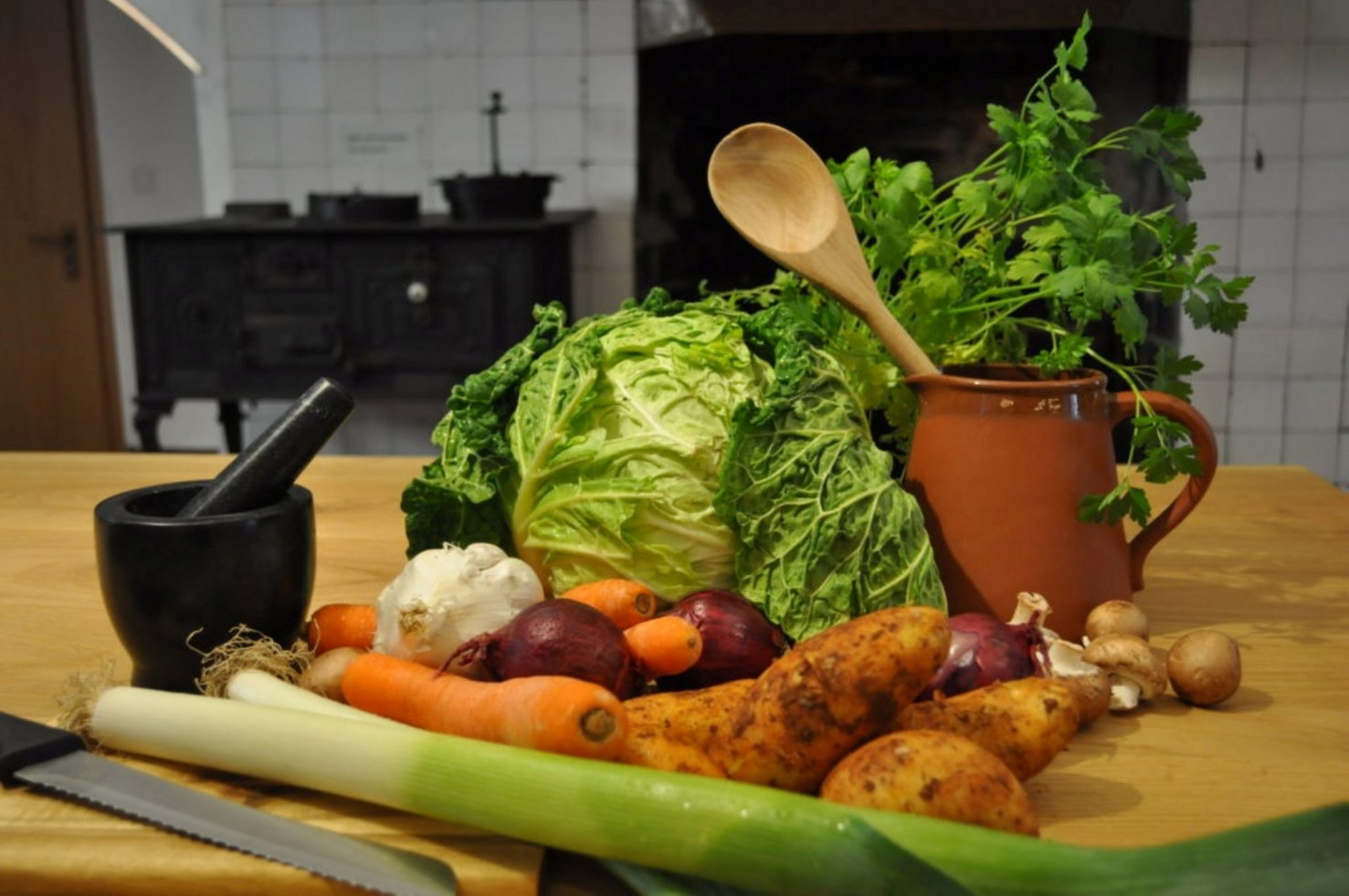 Auf einem Holztisch, der in einer Küche steht liegenverschiedene Gemüse wie Lauch, Möhre, Kartoffel und Zwiebel.