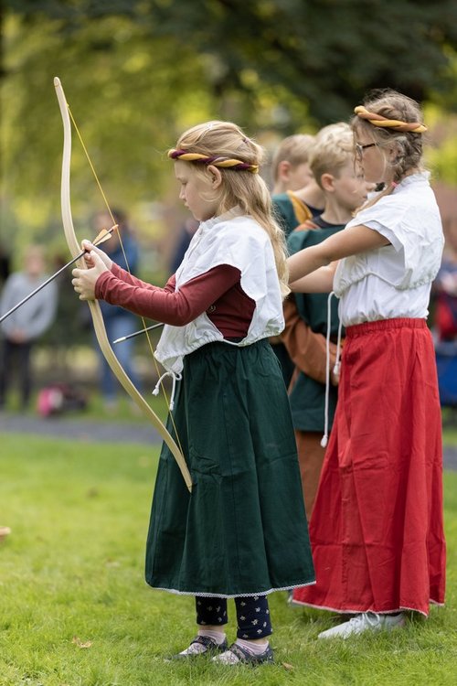 Kinder in mittelalterlicher Kleidung üben Bogenschießen beim Ritterlager an der Burg Vischering.
