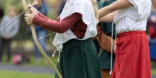 Kinder in mittelalterlicher Kleidung üben Bogenschießen beim Ritterlager an der Burg Vischering.