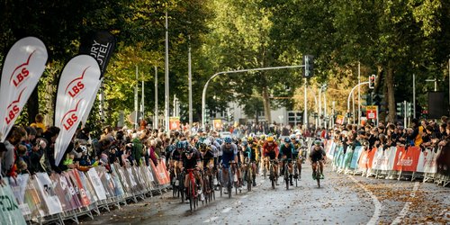 Radrennfahrerinnen und Radrennfahrer fahren beim Münsterland Giro vor jubelndem Publikum durchs Ziel.