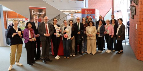 Mehrere Personen stehen im Foyer des Kreishauses vor Informationsständen zur Ausstellung „Gesichter des Ehrenamtes“ und posieren gemeinsam für ein Gruppenfoto.