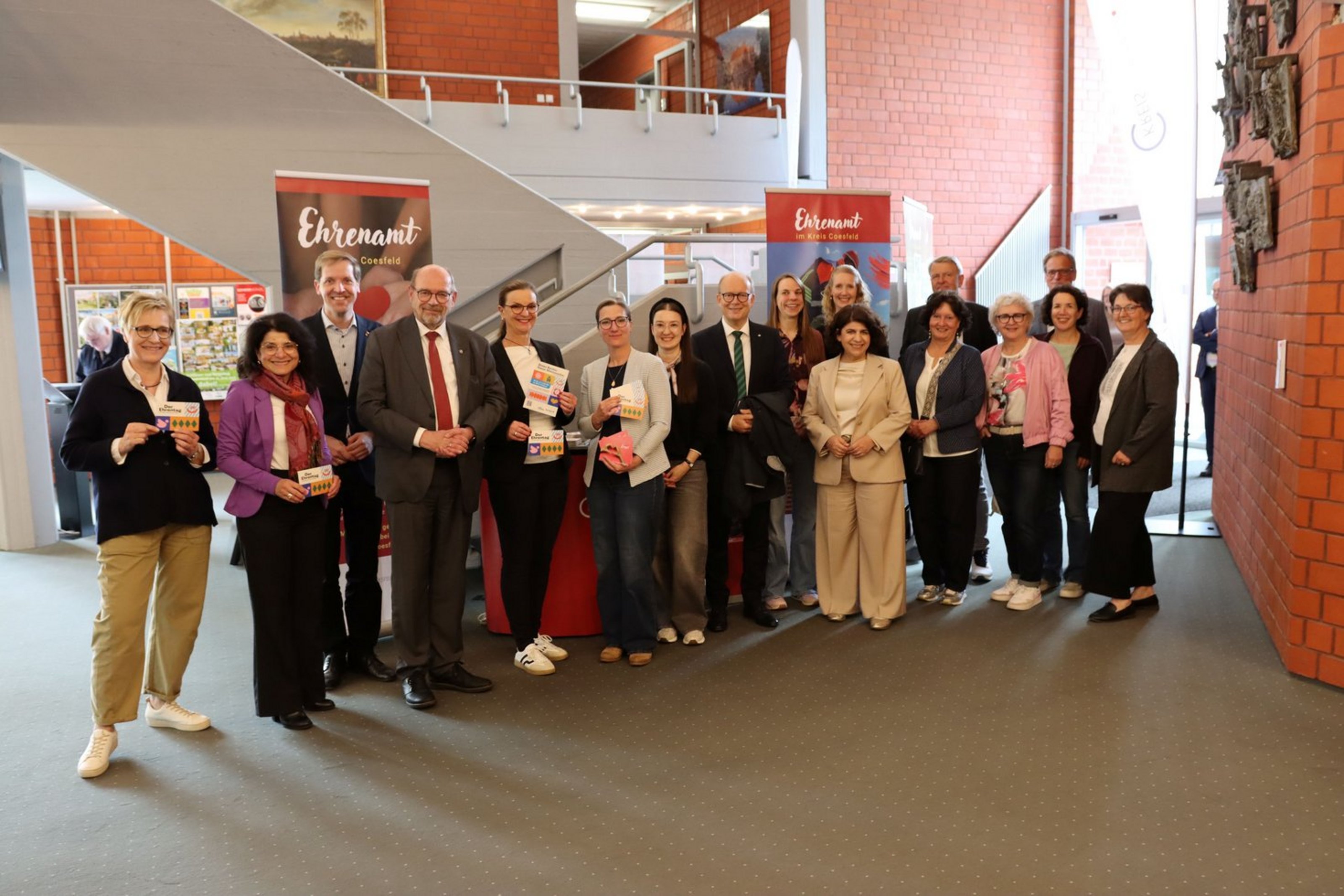 Mehrere Personen stehen im Foyer des Kreishauses vor Informationsständen zur Ausstellung „Gesichter des Ehrenamtes“ und posieren gemeinsam für ein Gruppenfoto.