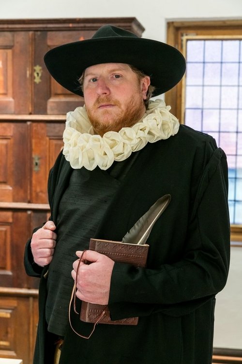 Ein Mann in historischem, schwarezn Gewand mit weißer Halskrause und Hut steht vor einem Holzschrank und hält ein Buch und eine Feder in der Hand.