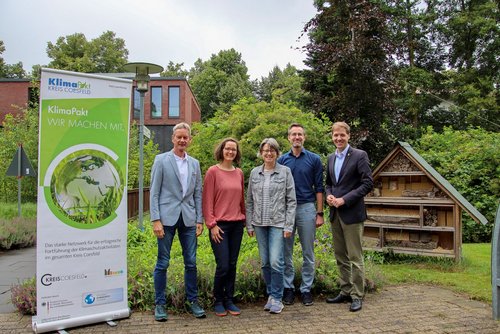 Fünf Personen stehen im Grünen neben einem KlimaPakt-Aufsteller und einem Insektenhotel.