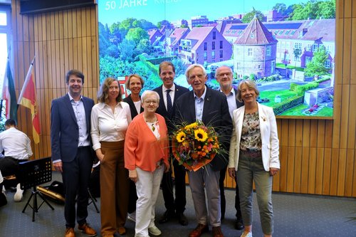 Acht Personen aus dem Vorstand des Kreisheimatvereins stehen im Großen Sitzungssaal beisammen. Ein Mann hält einen Blumenstrauß in der Hand. 