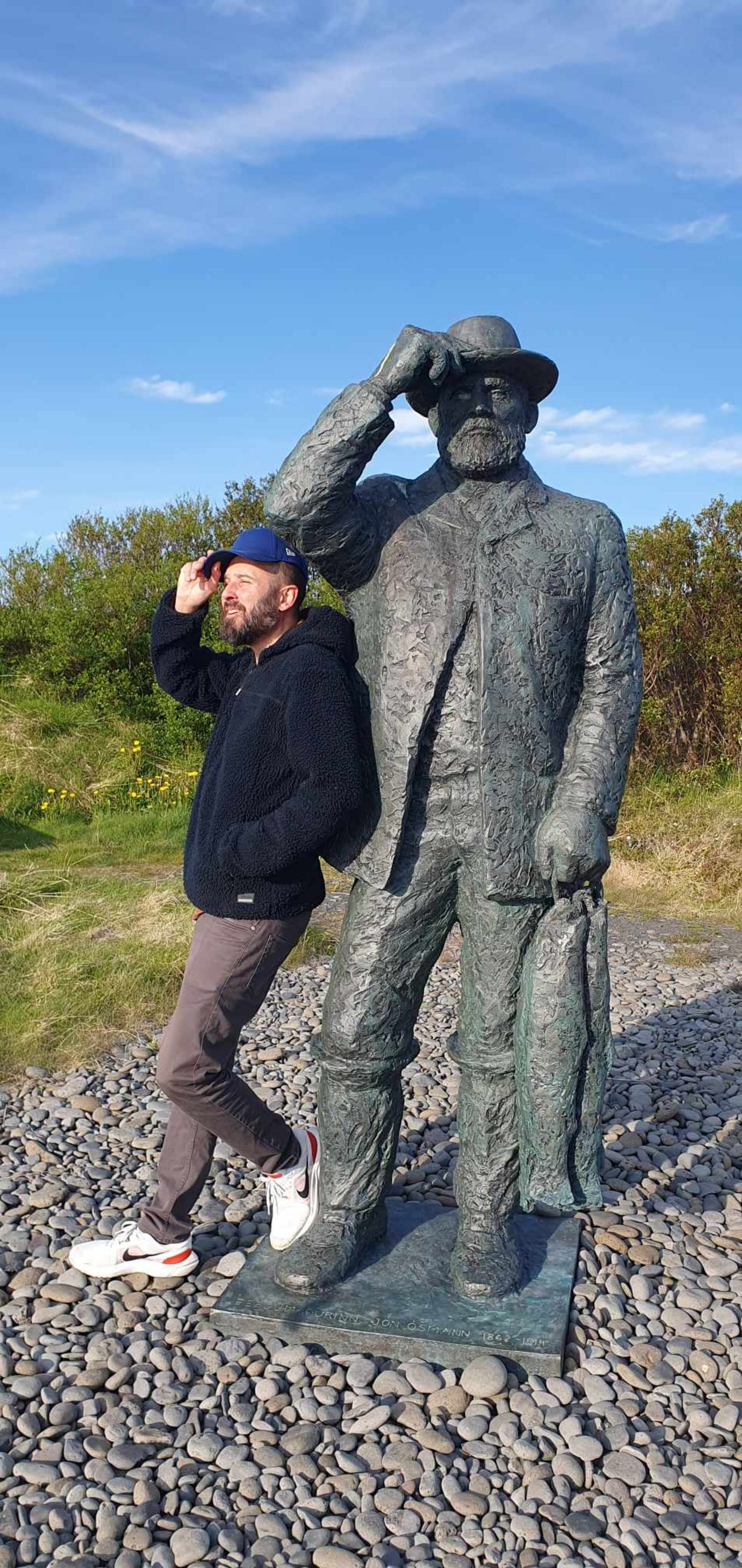 Joachim B. Schmidt auf Island an der Statue der titelgebenden Figur seines neuen Romans „Ósmann (Foto: Joachim B. Schmidt) Ein Mann steht neben einer großen Männerskulptur am Strand.