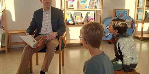 Landrat Dr. Schulze Pellengahr liest in einem Klassenzimmer mehreren Kindern aus einem Kinderbuch vor. 
