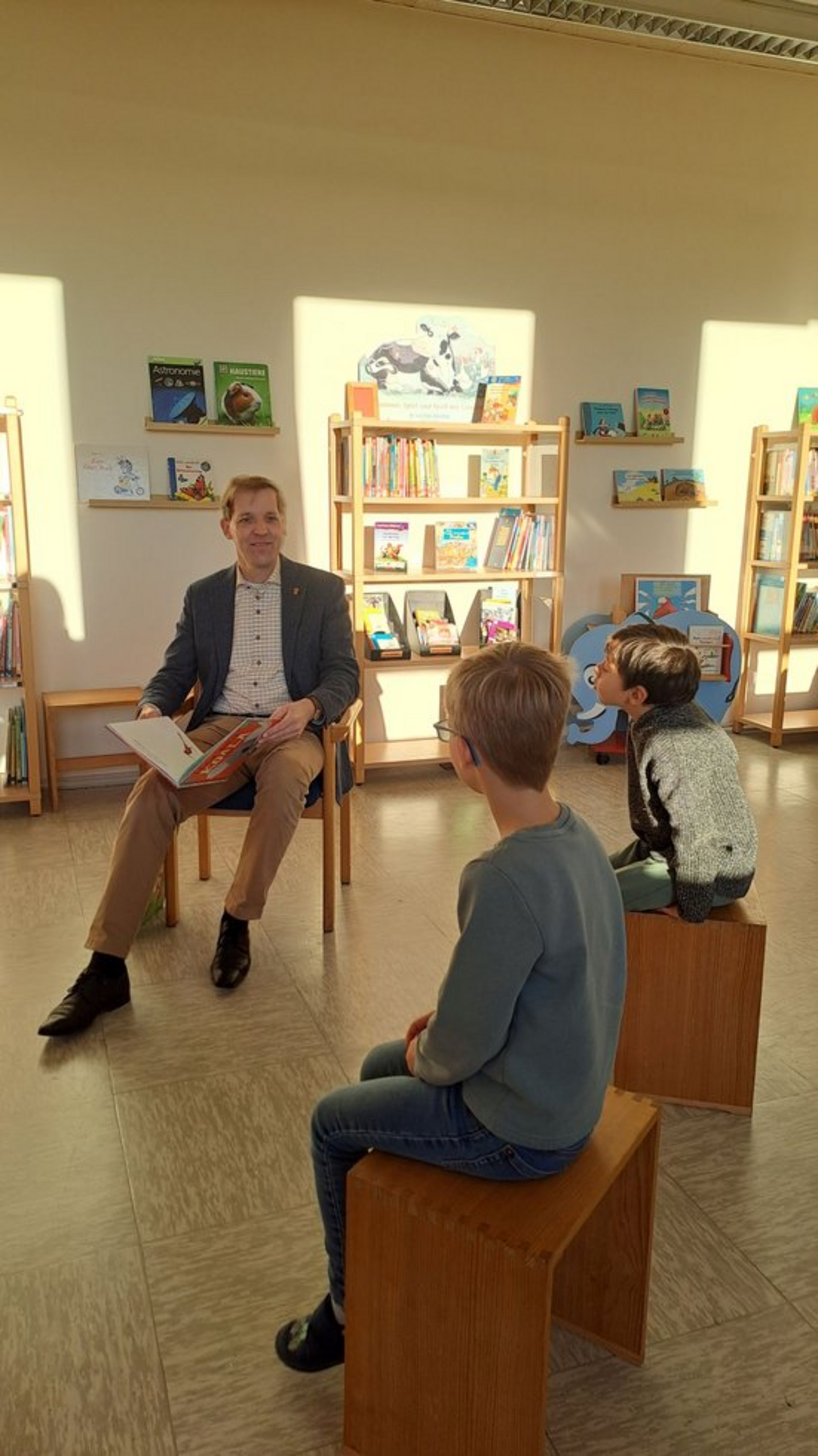 Landrat Dr. Christian Schulze Pellengahr liest in einem Klassenzimmer mehreren Kindern aus einem Kinderbuch vor.