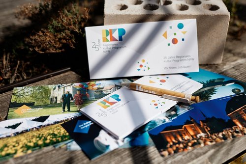 Auf einem Holzuntergrund liegen verschiedene Flyer-Karten des RKP Regionalem Kultur Programm NRW.