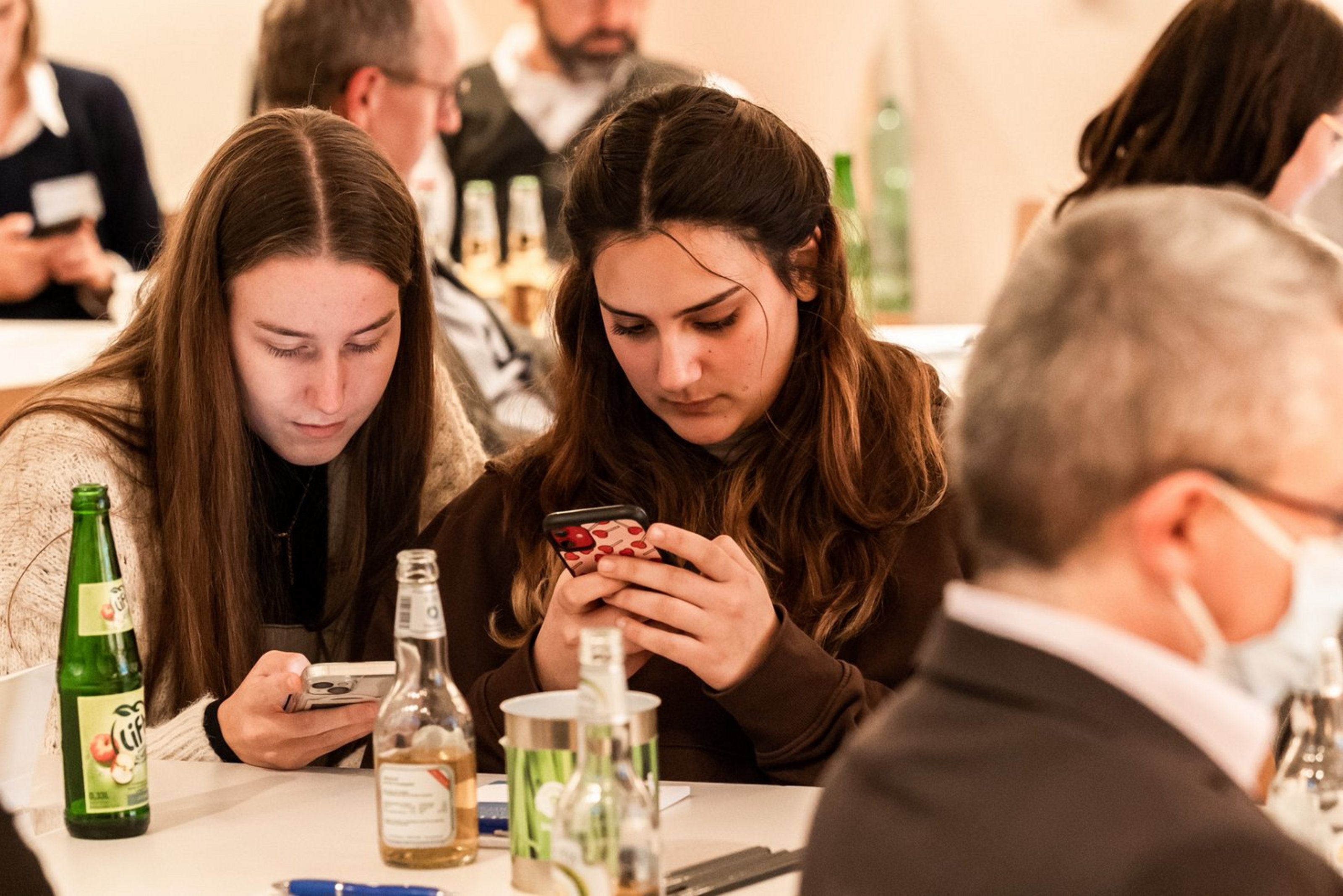 Zwei junge Frauen sitzen nebeneinander an einem Tisch und schauen auf ihre Smartphones