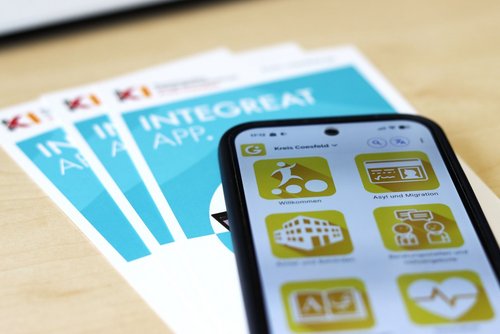 Smartphone mit geöffneter Integreat-App des Kreises Coesfeld neben Informationsflyern zur App.
