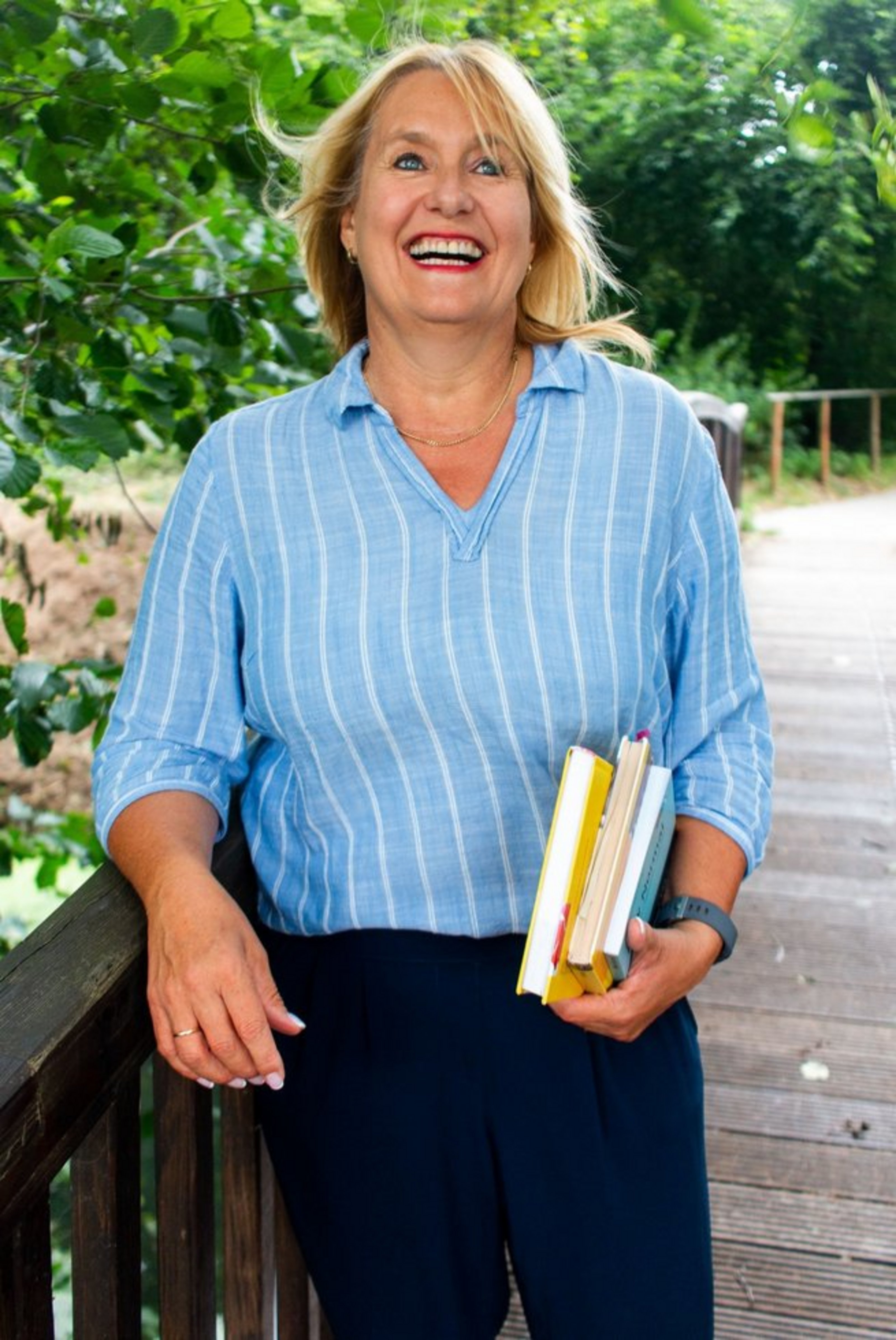 Eine FRau in blauer KLeidung steht an einem Geländer und lacht.