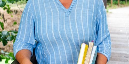 Eine FRau in blauer KLeidung steht an einem Geländer und lacht.