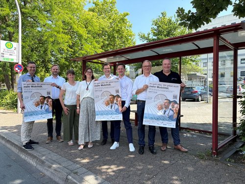 Acht Personen stehen an einer Bushaltestelle und präsentieren Plakate zur Verbesserung des ÖPNV in Datteln.