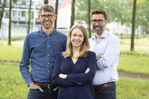 Drei Personen stehen draußen auf einer Wiese vor einer modernen Gebäudekulisse und blicken lächelnd in die Kamera. Links steht ein Mann mit Brille und Jeanshemd, in der Mitte eine Frau mit blonden Haaren und dunkelblauer Bluse, rechts ein weiterer Mann mit Brille, hellem Hemd. Von links nach rechts sind dies: Lars Krolik, Laura Säumenicht und Andre Sebastian vom Kulturbüro des Münsterland e.V. 
