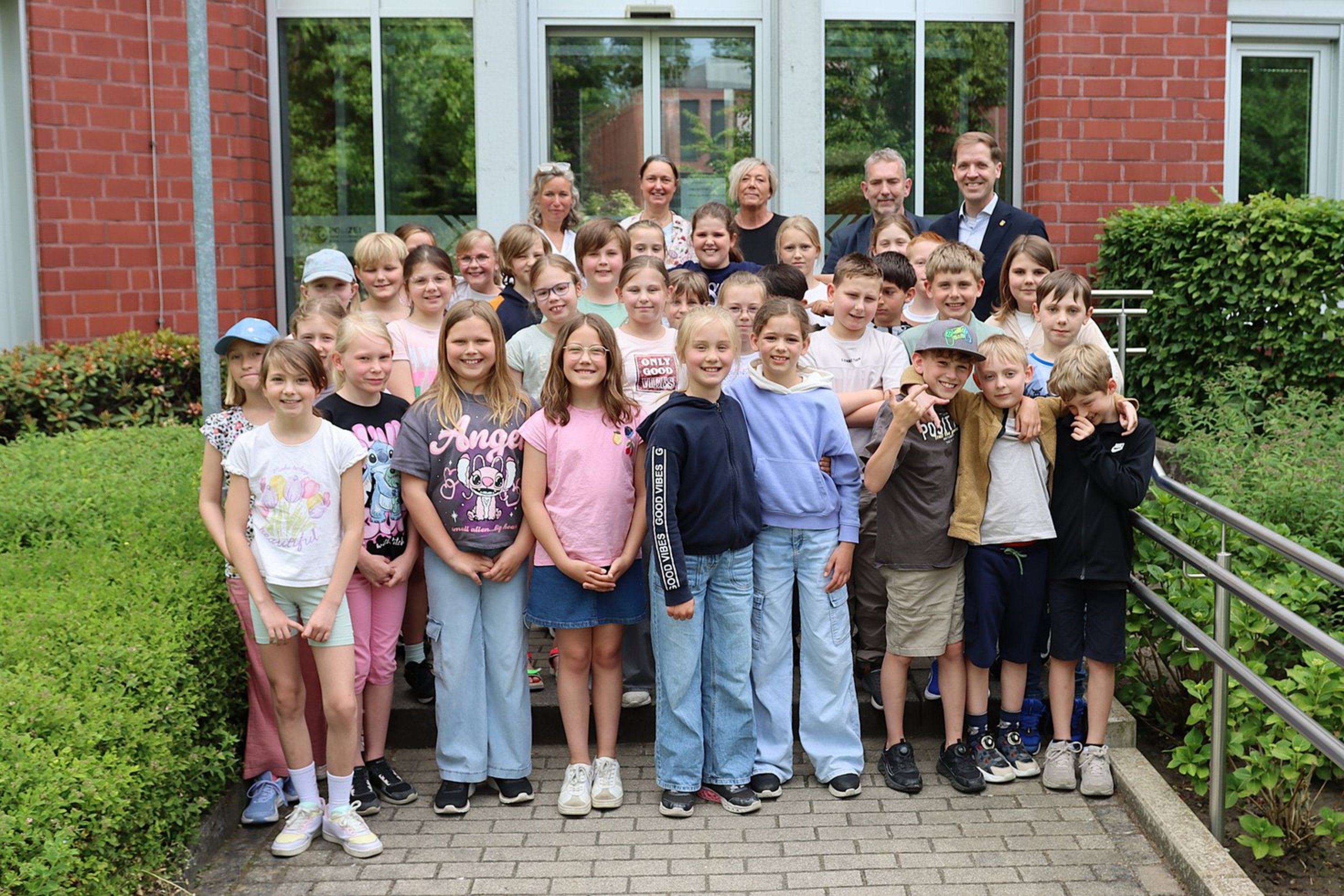 Eine Gruppe von rund 20 Kindern steht vor dem Eingang eines Gebäudes aus rotem Stein. In der hinteren Reihe stehen drei Frauen und zwei Männer