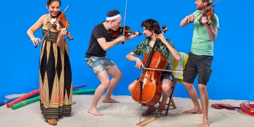Die vier Musikerinnen und Musiker des Feuerbach Quartetts musizieren barfuß und sommerlich gekleidet im Sand vor blauem Hintergrund.