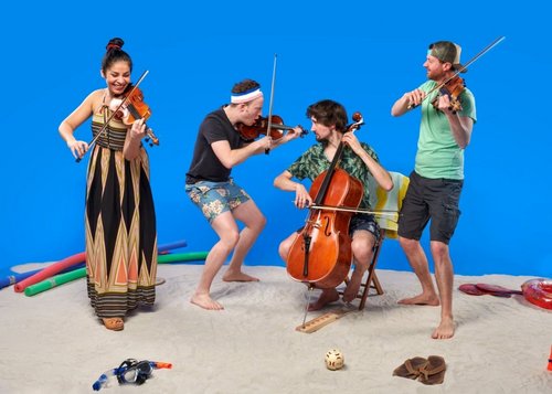 Die vier Musikerinnen und Musiker des Feuerbach Quartetts musizieren barfuß und sommerlich gekleidet im Sand vor blauem Hintergrund.