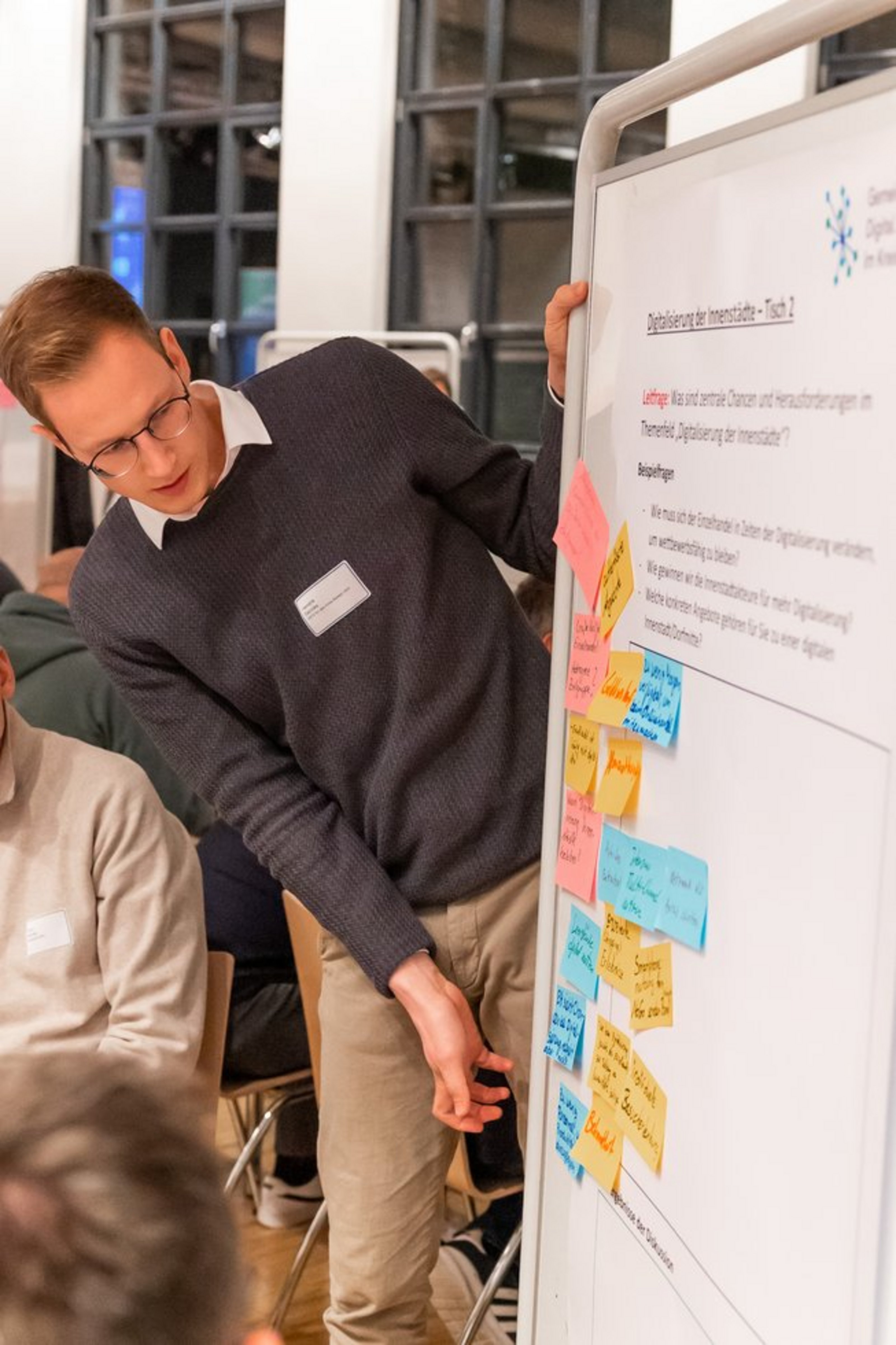 Zwei Männer stehen vor einem Whiteboard mit farbigen Haftnotizen und Text