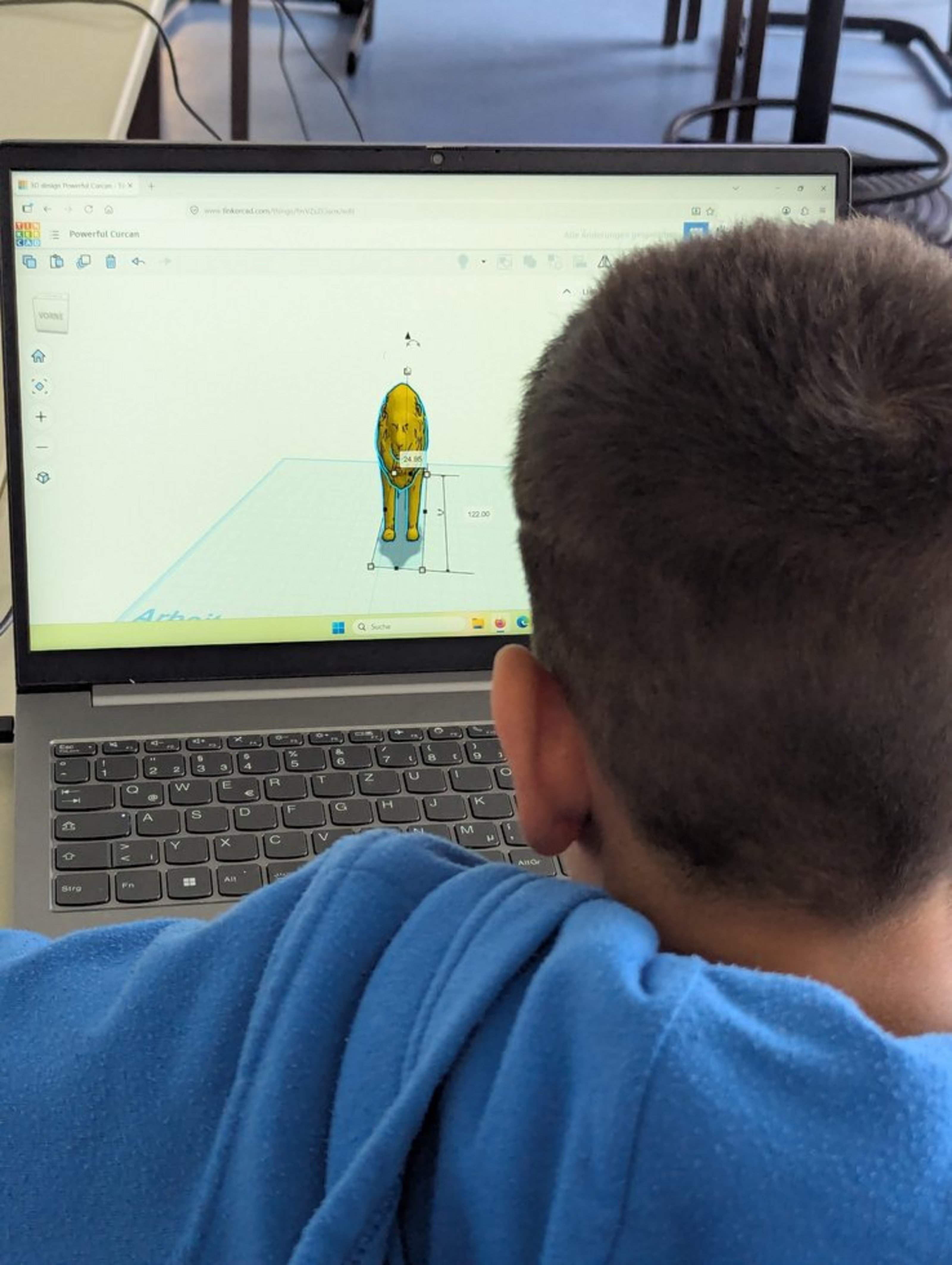 Ein Kind mit kurzen Haaren sitzt vor einem Laptop, auf dem ein Tier zu sehen ist. Das Kind ist von hinten zu sehen.