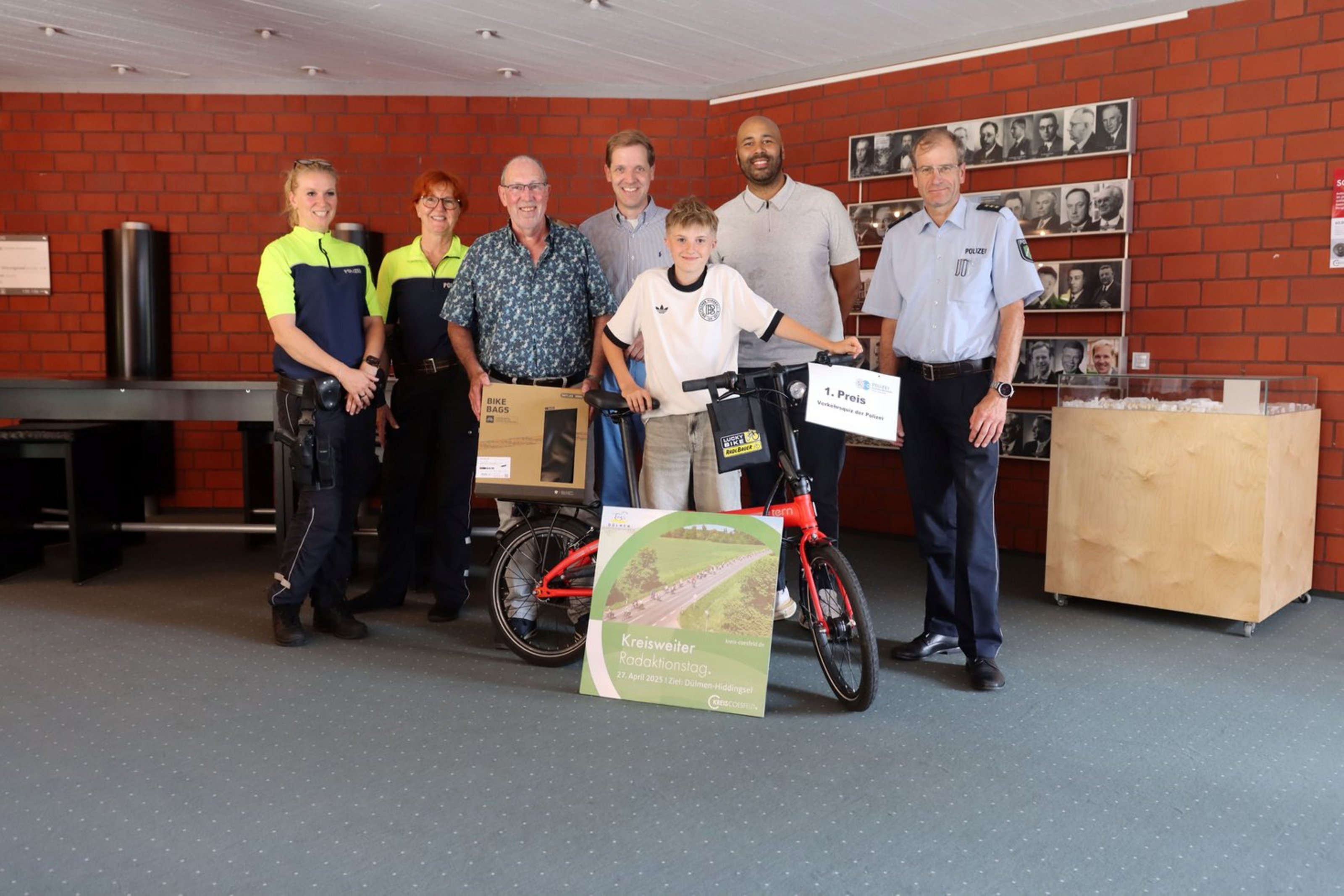 Junge mit rotem Fahrrad und Erwachsene bei Preisverleihung im Kreishaus, darunter Polizei und Veranstalter.